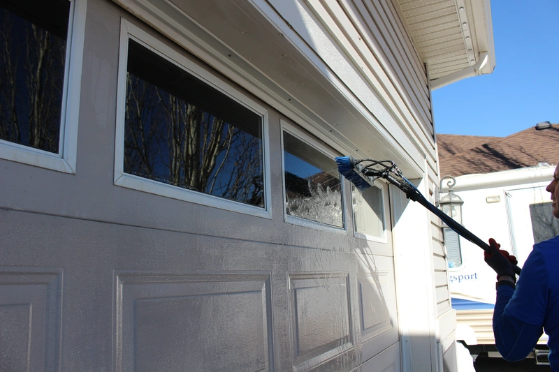 Professional window cleaner using a specialized brush to clean the windows of a residential garage door, emphasizing the detail-oriented service provided by A Touch Of Glass in Calgary.