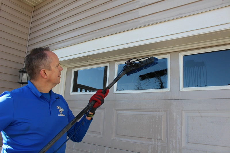 A professional window cleaner from A Touch Of Glass cleans a garage door window with a long-handled brush, highlighting expert exterior cleaning services in Calgary, Alberta.